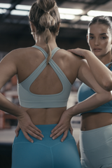 Woman in a blue sports bra and leggings looking at herself in a mirror.