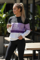 Woman wearing a Hustle Sportswear sweatshirt holding a coffee cup outdoors.