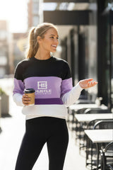 Woman wearing a black, purple, and white sweatshirt with 'Hustle' logo outdoors.