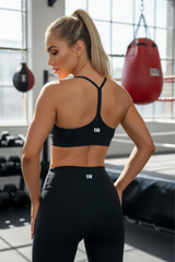 Woman in black sports bra and leggings standing in a gym.