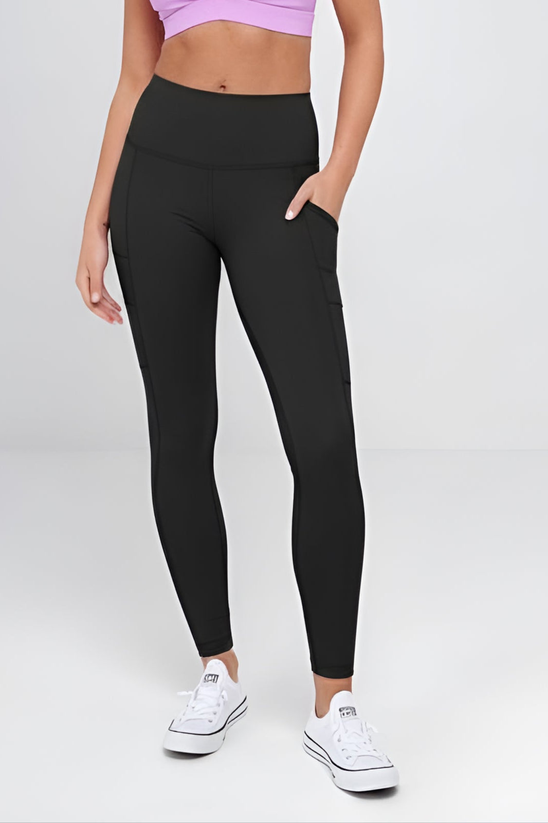 Woman wearing a purple sports bra and black leggings on a white background Woman wearing a purple sports bra and black leggings on a white background