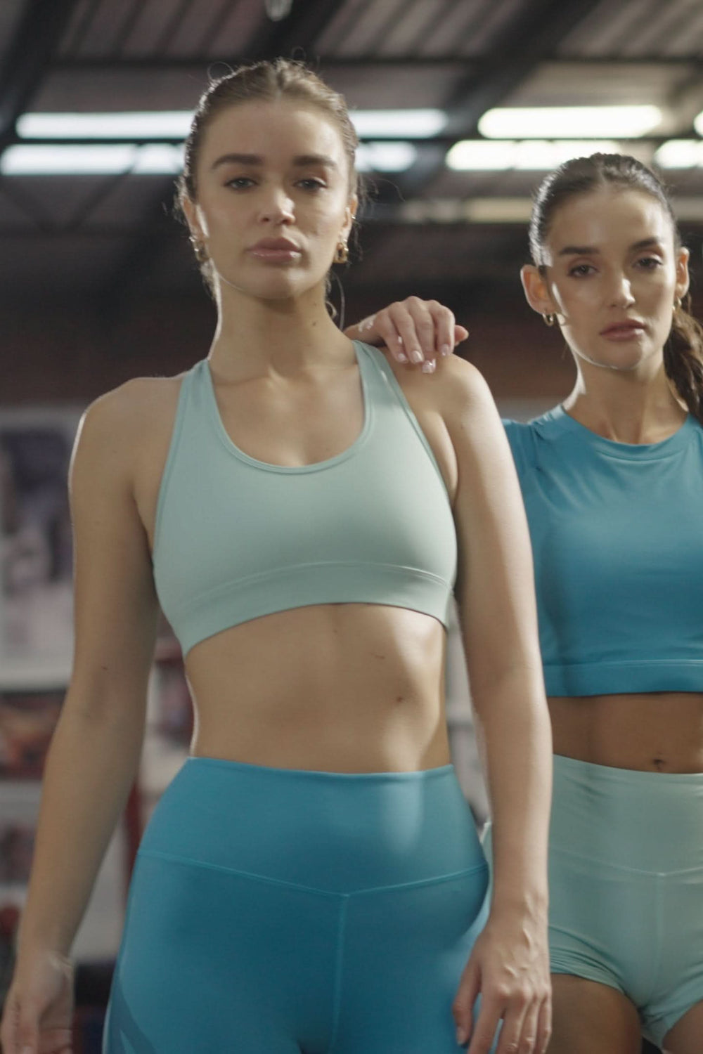 Two women in matching blue athletic wear standing in a boxing ring.