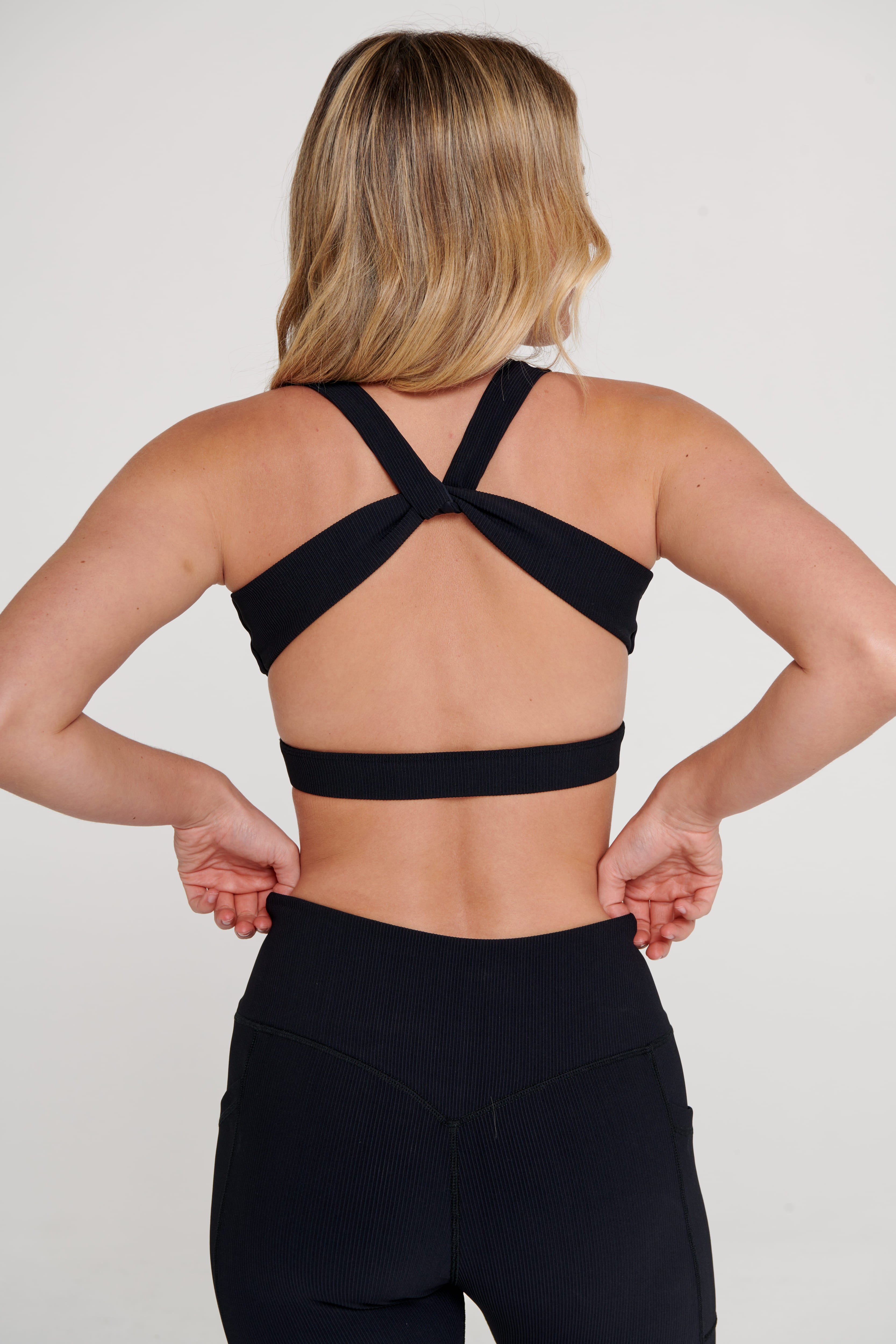 Person wearing a black sports bra and leggings on a plain background