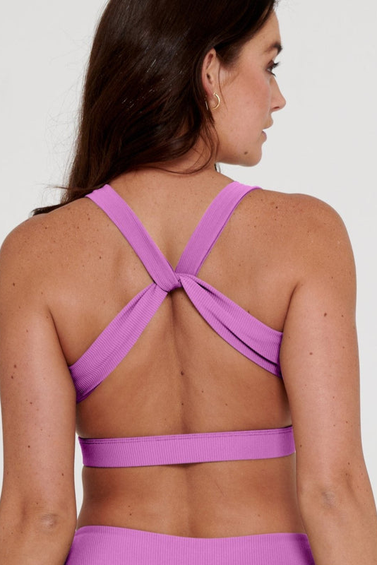 Woman wearing a purple sports bra and leggings on a white background