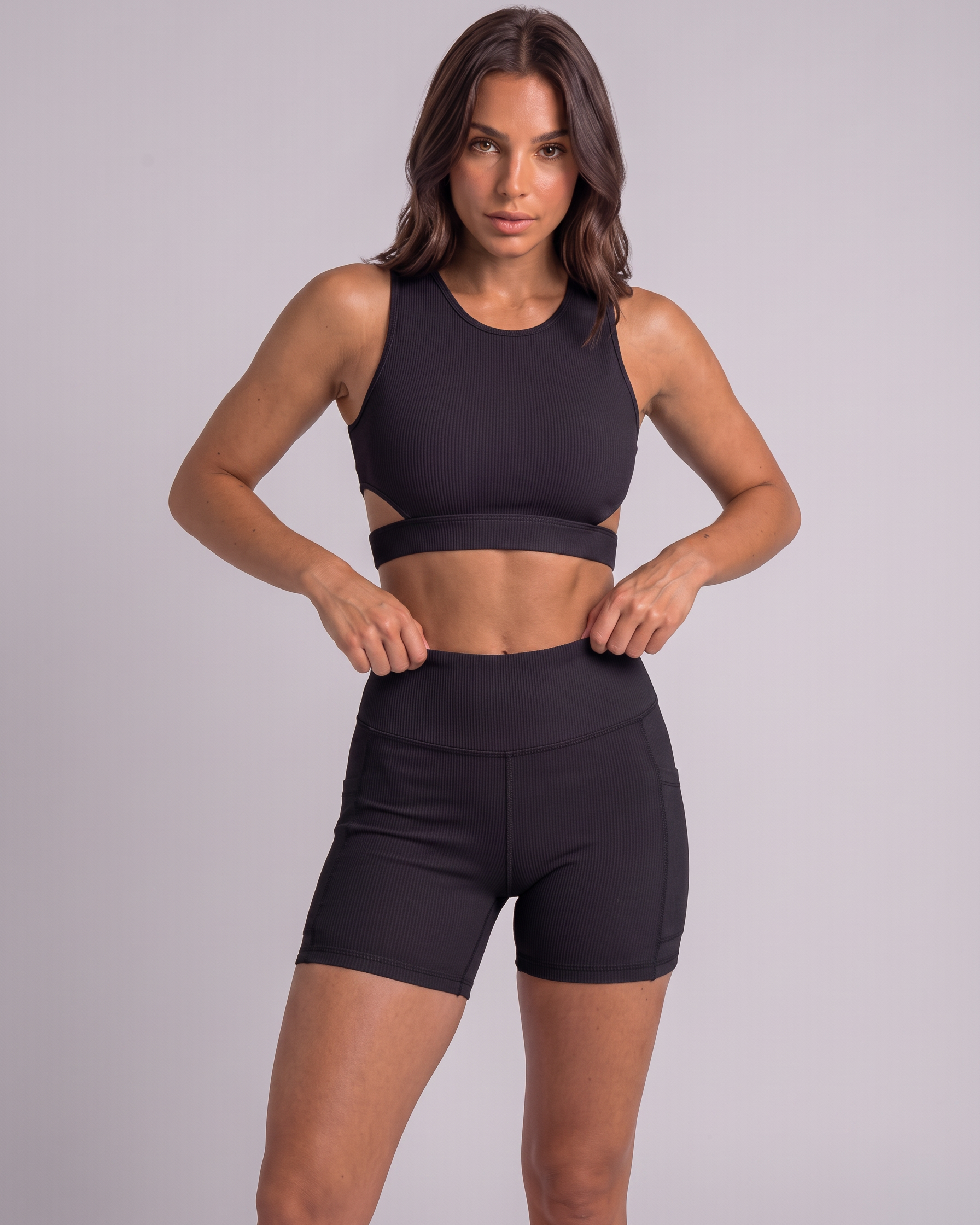 A woman modeling a black athletic crop top and matching high-waisted shorts against a solid light gray studio background.